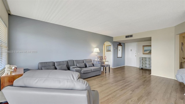 living room featuring a textured ceiling, visible vents, arched walkways, and wood finished floors