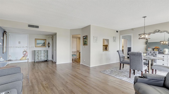 living room featuring light wood-style floors, visible vents, a textured ceiling, and an inviting chandelier