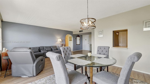 dining room featuring arched walkways, a textured ceiling, light wood-style flooring, visible vents, and baseboards