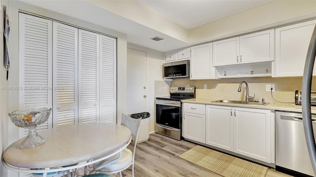 kitchen featuring open shelves, visible vents, light wood-style flooring, appliances with stainless steel finishes, and a sink