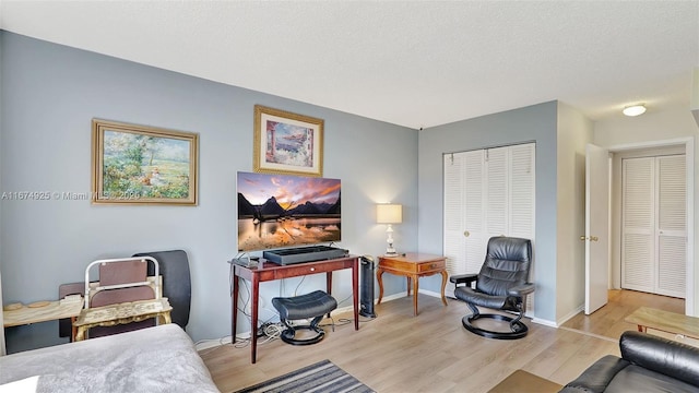 sitting room with light wood-style flooring, baseboards, and a textured ceiling