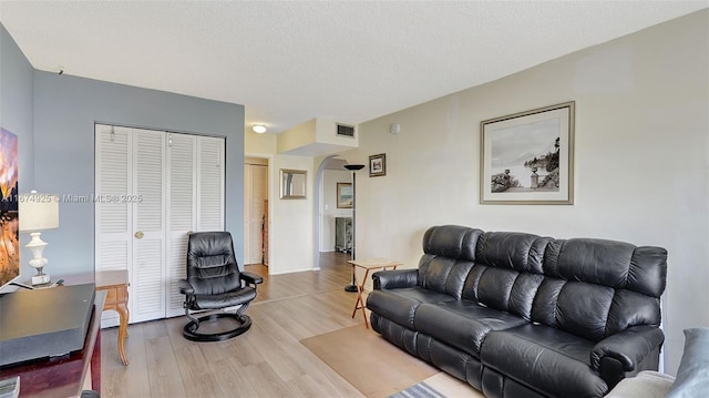 living area featuring a textured ceiling, visible vents, arched walkways, and wood finished floors