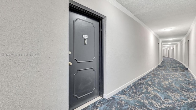 hall featuring a textured wall, a textured ceiling, and baseboards