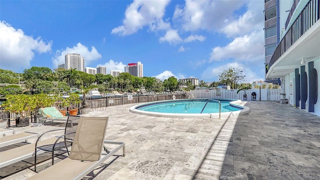 pool with a patio area, fence, and a city view