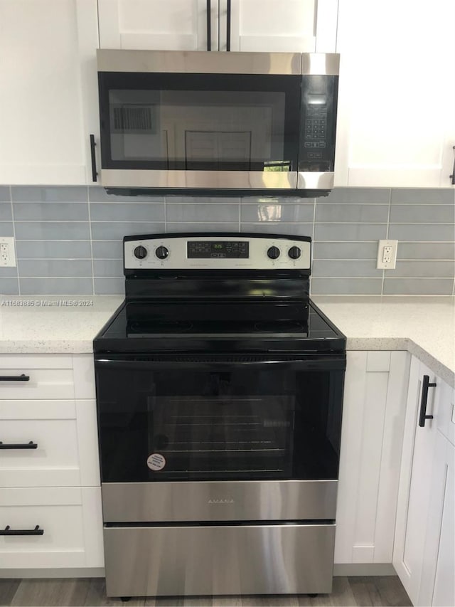 kitchen featuring light stone counters, backsplash, appliances with stainless steel finishes, white cabinets, and light wood-type flooring