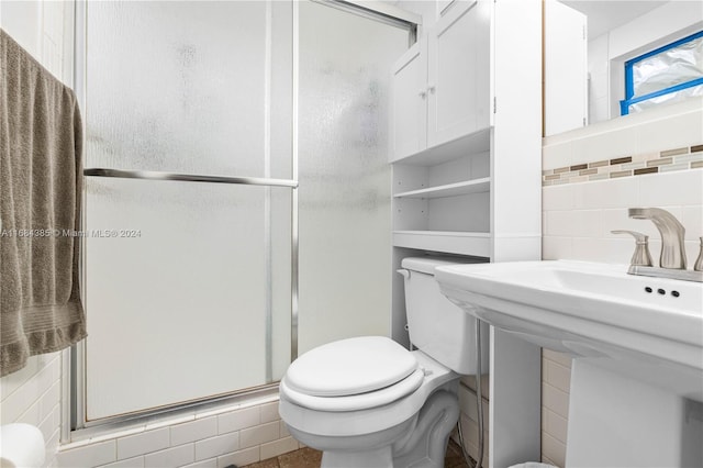 bathroom with toilet, a shower with shower door, sink, tile walls, and tasteful backsplash