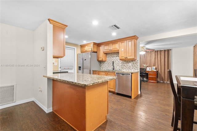 kitchen with light stone countertops, kitchen peninsula, ceiling fan, stainless steel appliances, and dark hardwood / wood-style floors