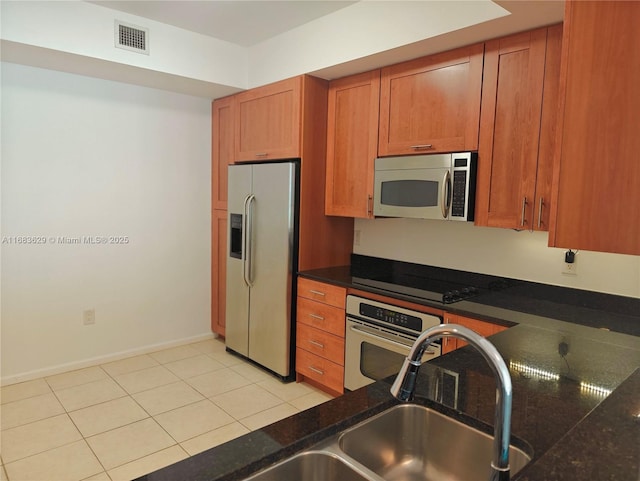 kitchen with sink, light tile patterned floors, stainless steel appliances, and dark stone counters