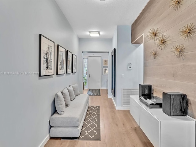 hallway featuring light hardwood / wood-style floors, a textured ceiling, and wooden walls