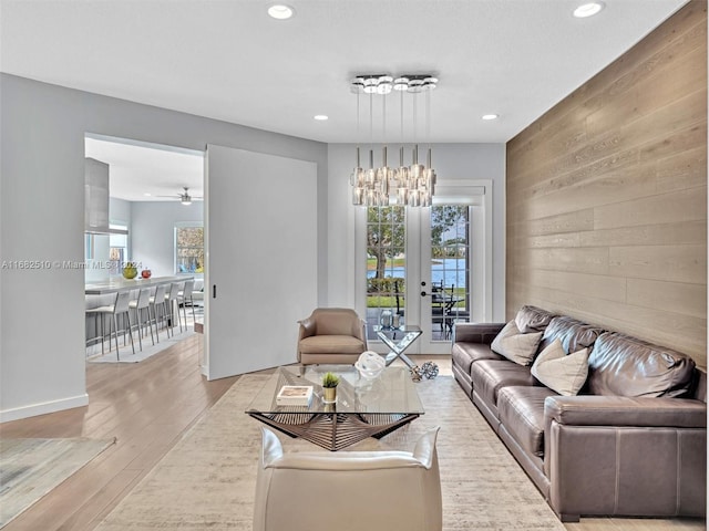 living room featuring french doors, ceiling fan, light wood-type flooring, and wood walls