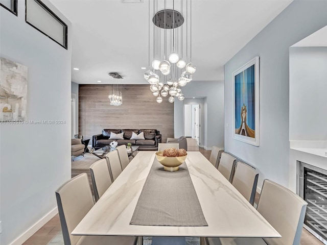 dining room with wood walls, a chandelier, beverage cooler, and light wood-type flooring