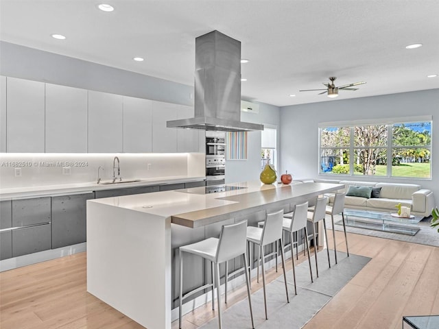 kitchen with island range hood, a kitchen island, light hardwood / wood-style flooring, sink, and white cabinets