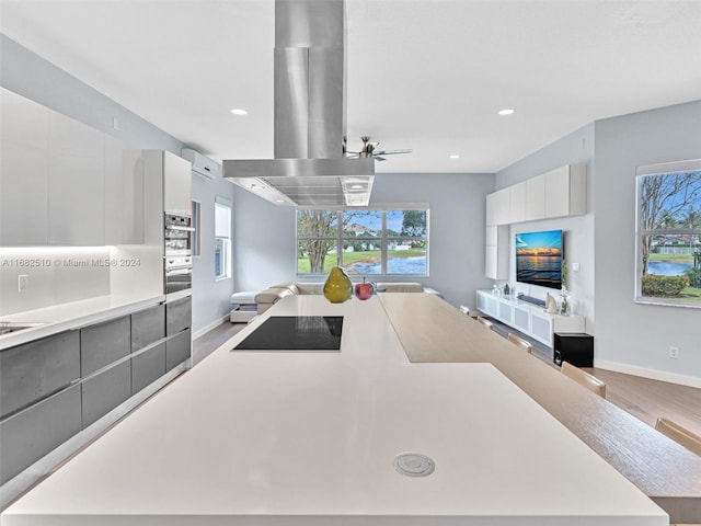 kitchen with island exhaust hood, white cabinets, plenty of natural light, and light wood-type flooring