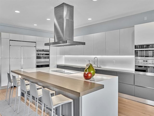 kitchen with stainless steel double oven, island range hood, black electric cooktop, light hardwood / wood-style floors, and paneled refrigerator