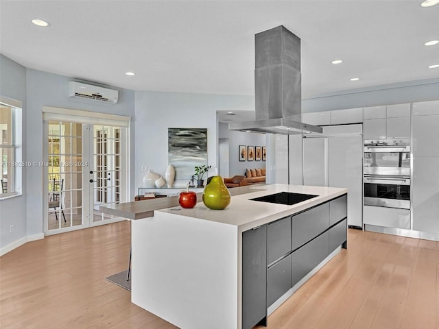 kitchen with gray cabinetry, a kitchen island, island exhaust hood, black electric cooktop, and light hardwood / wood-style flooring