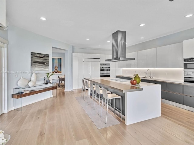 kitchen with sink, light wood-type flooring, a kitchen island, white cabinetry, and extractor fan