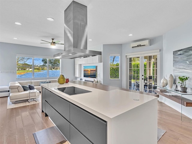 kitchen with a spacious island, island range hood, a wall mounted air conditioner, black electric stovetop, and a water view