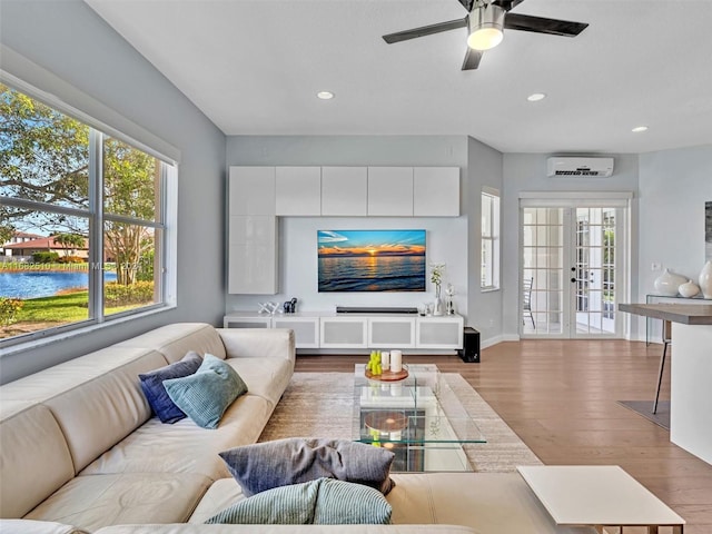 living room with french doors, light hardwood / wood-style flooring, a wall mounted air conditioner, a water view, and ceiling fan