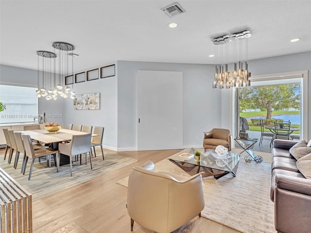 living room featuring an inviting chandelier, a water view, and light wood-type flooring