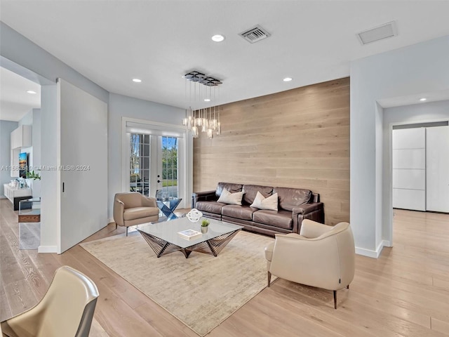 living room featuring light hardwood / wood-style floors, french doors, wood walls, and a chandelier