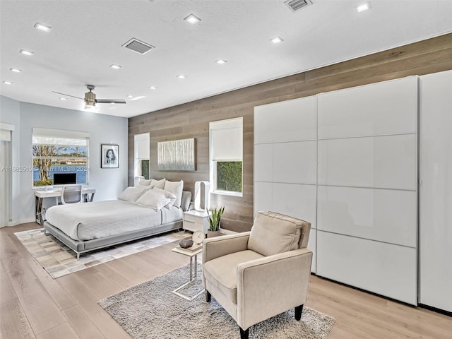 bedroom featuring ceiling fan, a textured ceiling, light wood-type flooring, and wooden walls