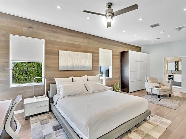 bedroom with light hardwood / wood-style flooring, ceiling fan, and wood walls