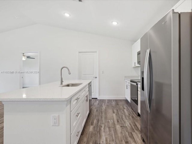 kitchen with appliances with stainless steel finishes, vaulted ceiling, white cabinets, hardwood / wood-style flooring, and a kitchen island with sink