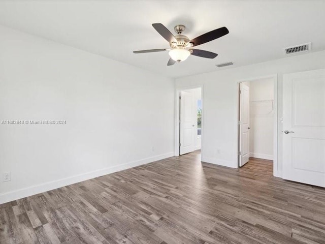 unfurnished bedroom featuring a spacious closet, hardwood / wood-style floors, a closet, and ceiling fan