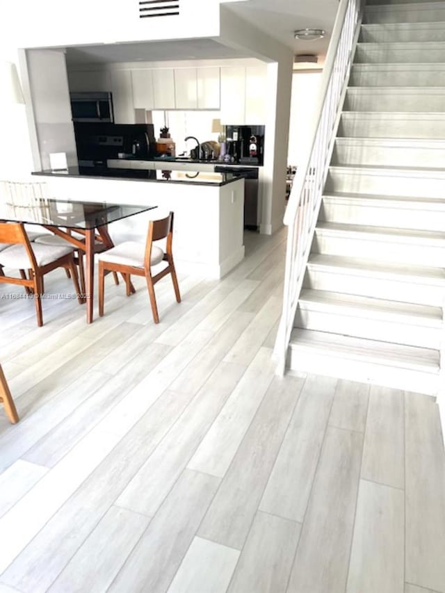 265 Grapetree Dr Unit 108, Key Biscayne, FL 33149 - kitchen with appliances with stainless steel finishes, dark countertops, white cabinetry, light wood-style flooring, and a sink