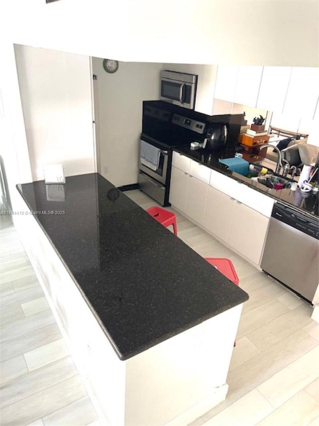 kitchen with stainless steel appliances, sink, white cabinets, and light wood-type flooring