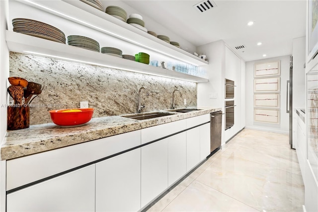 kitchen with light stone counters, stainless steel dishwasher, backsplash, sink, and white cabinetry