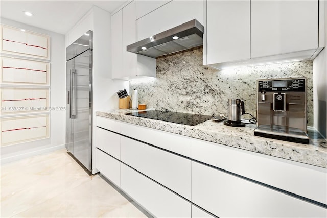 kitchen with light stone counters, white cabinetry, stainless steel built in refrigerator, wall chimney exhaust hood, and black electric cooktop