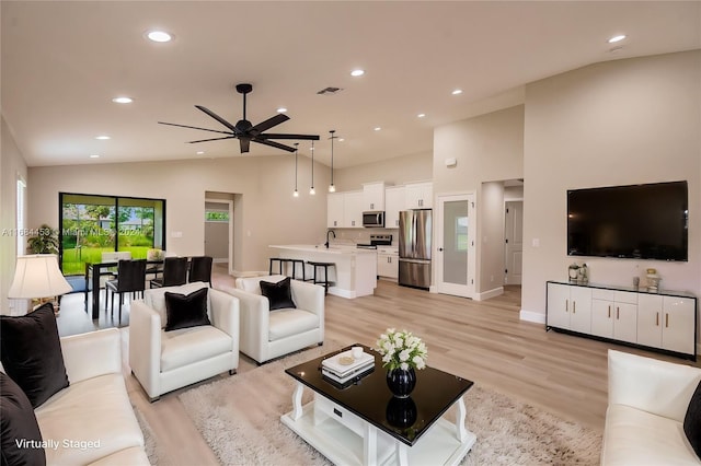 living room with light hardwood / wood-style floors, ceiling fan, sink, and vaulted ceiling