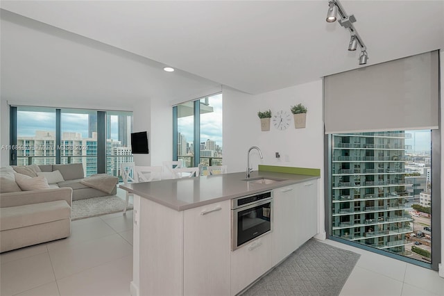 kitchen with stainless steel oven, kitchen peninsula, sink, light tile patterned floors, and white cabinetry