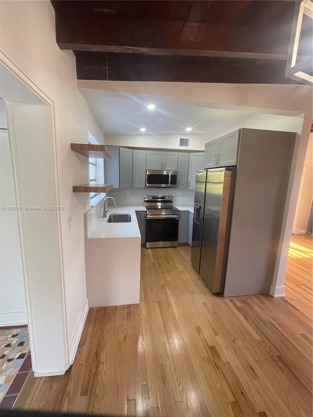 kitchen with beam ceiling, gray cabinetry, stainless steel appliances, sink, and light hardwood / wood-style floors