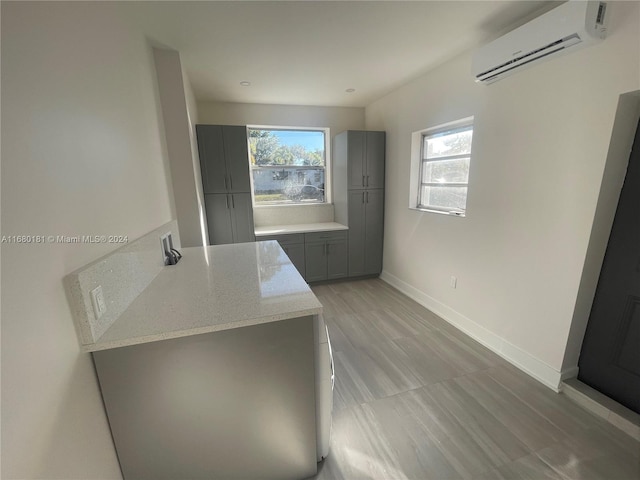 interior space with gray cabinets, a wall mounted AC, light stone counters, and plenty of natural light