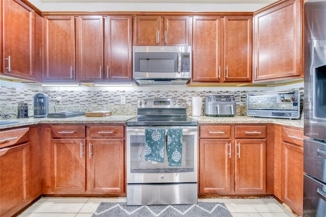 kitchen with light stone counters, tasteful backsplash, appliances with stainless steel finishes, and light tile patterned floors