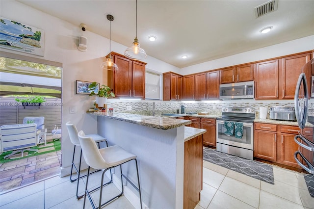 kitchen with appliances with stainless steel finishes, kitchen peninsula, pendant lighting, light stone counters, and a breakfast bar