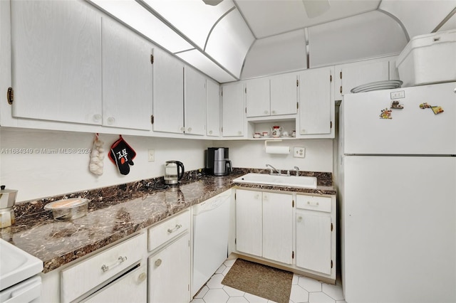 kitchen with dark stone countertops, sink, light tile patterned floors, white cabinetry, and white appliances