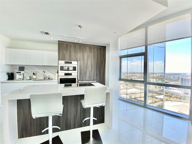 kitchen with decorative backsplash, light tile patterned floors, a breakfast bar area, white cabinetry, and double oven