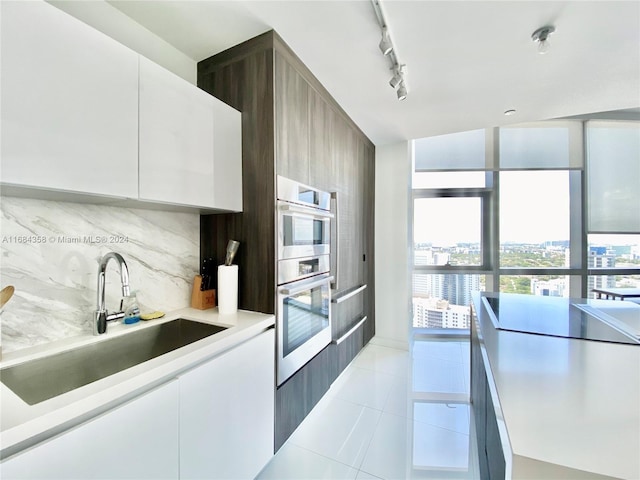 kitchen with tasteful backsplash, rail lighting, white cabinetry, light tile patterned flooring, and sink