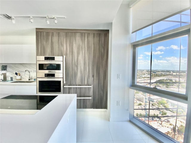 kitchen featuring decorative backsplash, white cabinets, light tile patterned flooring, sink, and stainless steel double oven