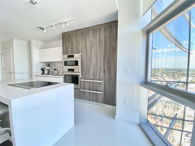 kitchen with black electric stovetop, backsplash, double oven, white cabinets, and light tile patterned floors