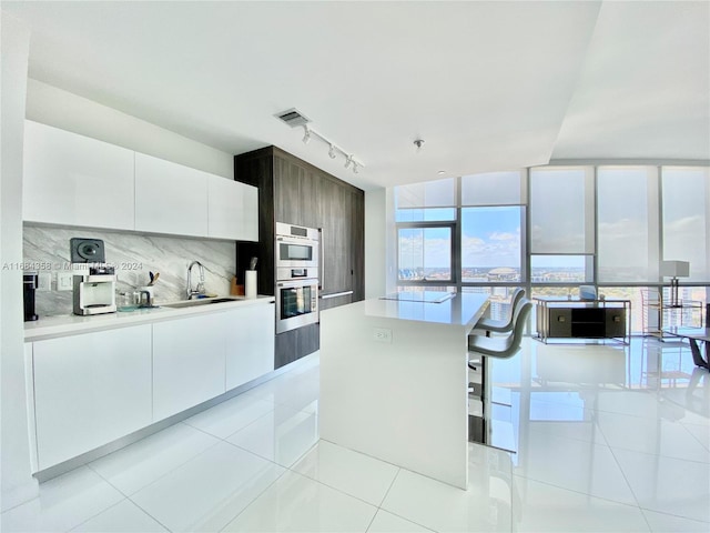 kitchen with backsplash, white cabinetry, light tile patterned flooring, sink, and a center island