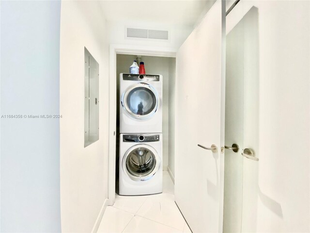 clothes washing area featuring electric panel, light tile patterned flooring, and stacked washing maching and dryer