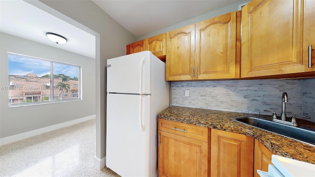 kitchen with dark stone counters, sink, tasteful backsplash, and white refrigerator