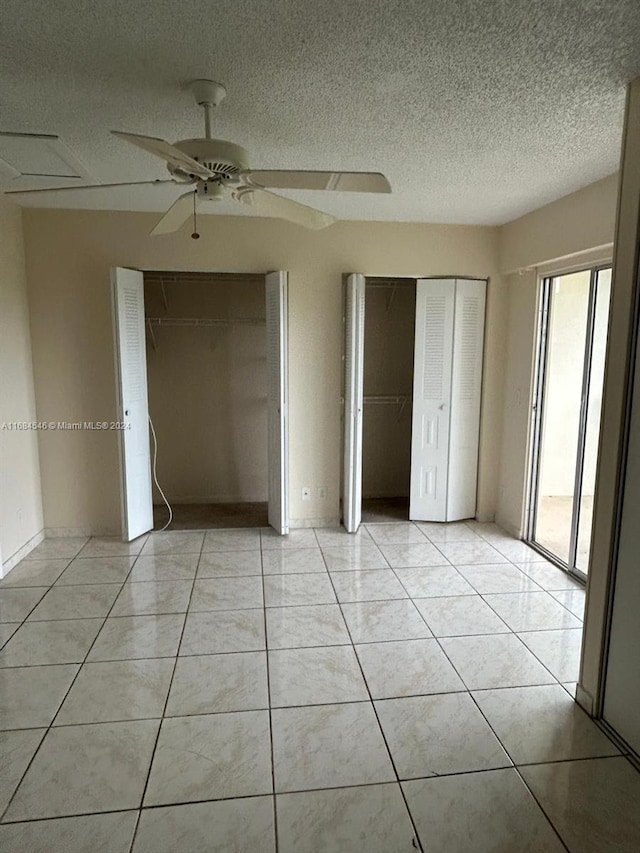 unfurnished bedroom with ceiling fan, a textured ceiling, light tile patterned floors, and two closets