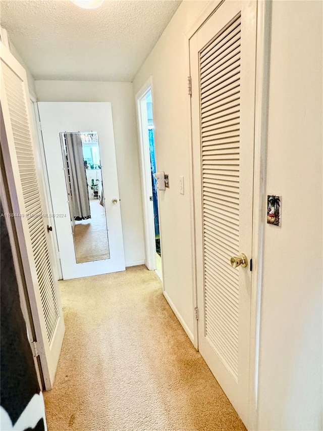 hall with light carpet and a textured ceiling