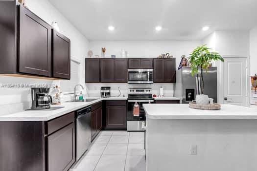 kitchen featuring sink, light tile patterned flooring, a kitchen island, stainless steel appliances, and dark brown cabinetry