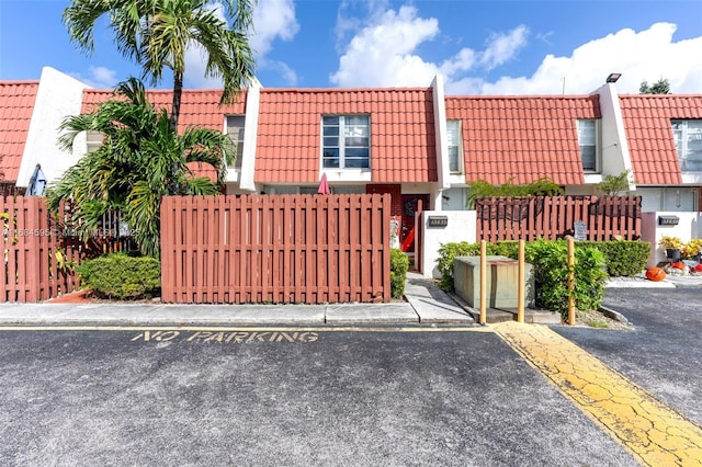 view of front facade with a tiled roof, fence, and uncovered parking